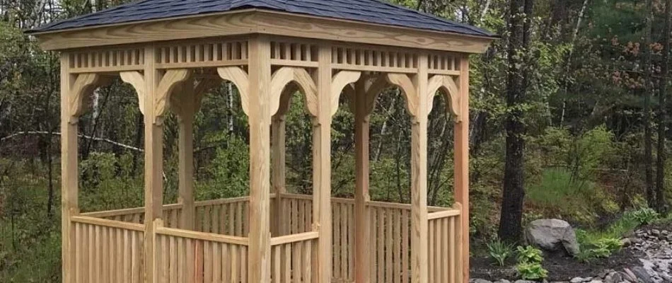 Wooden gazebo with plants in background.